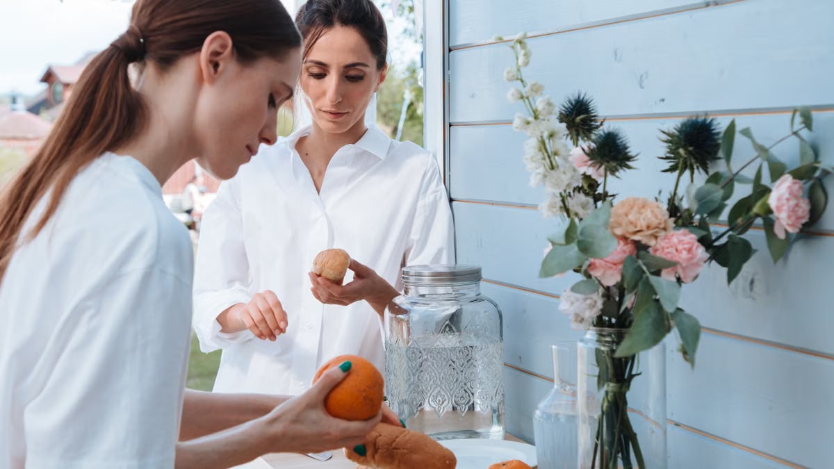 Two women arranging bread and flowers on a table outdoors, creating a serene setting.